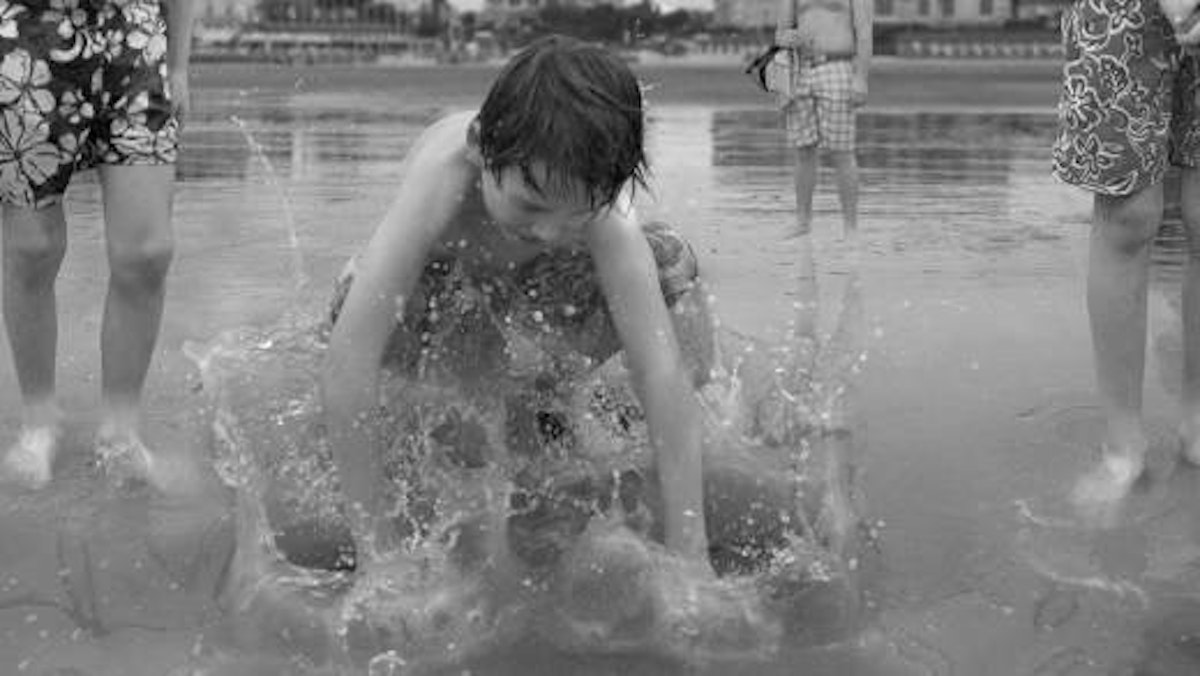 A child splashes in the water in-between two adults